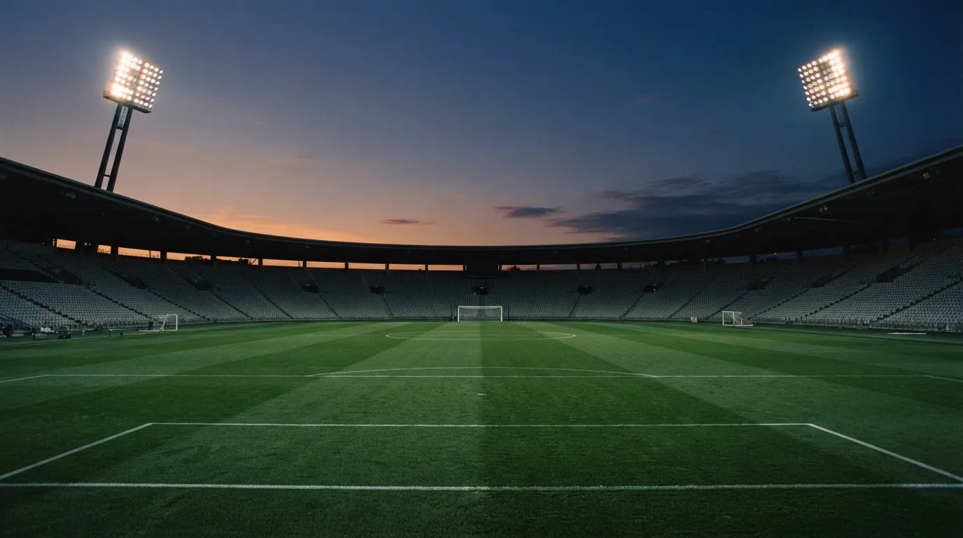 An empty football stadium with floodlight masts at dusk