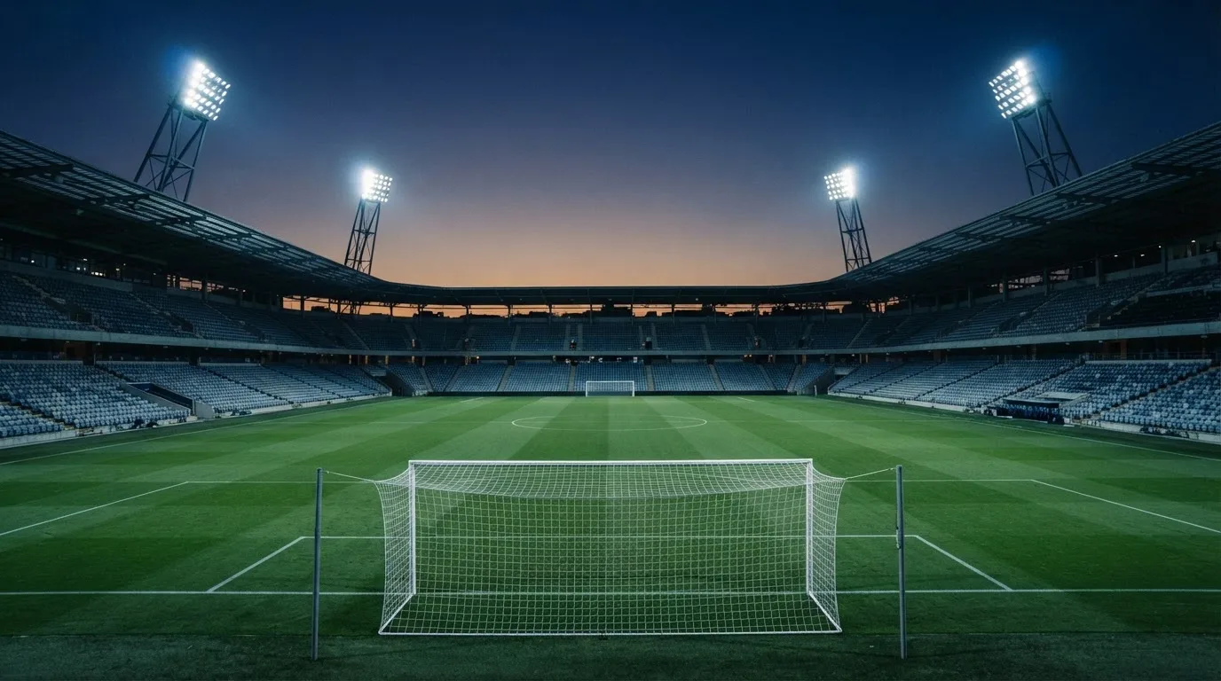 An empty football stadium with floodlight masts at dusk