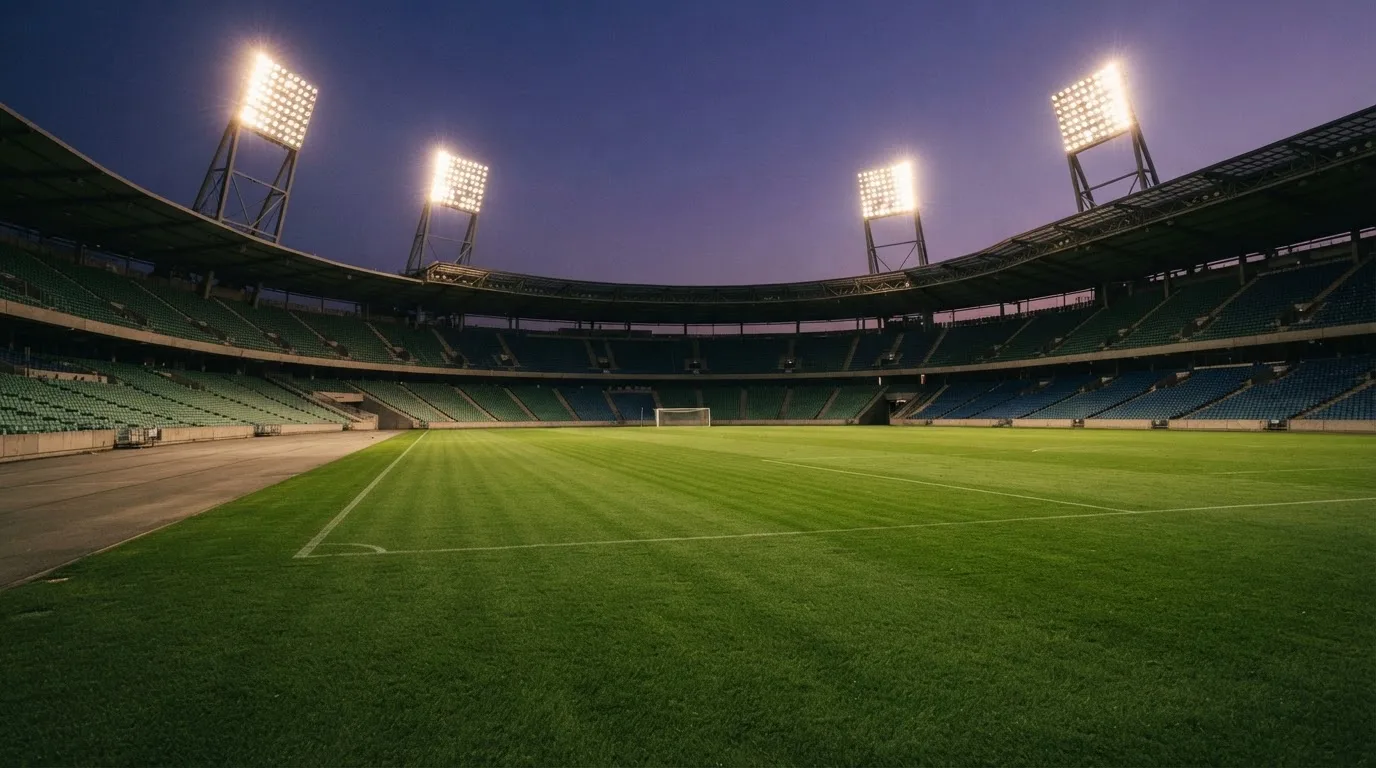 An empty football stadium with floodlight masts at dusk