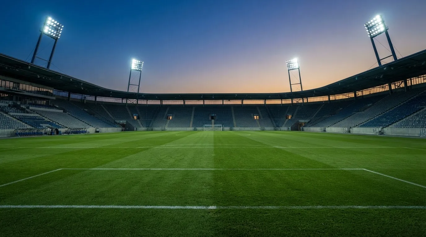 An empty football stadium with floodlight masts at dusk