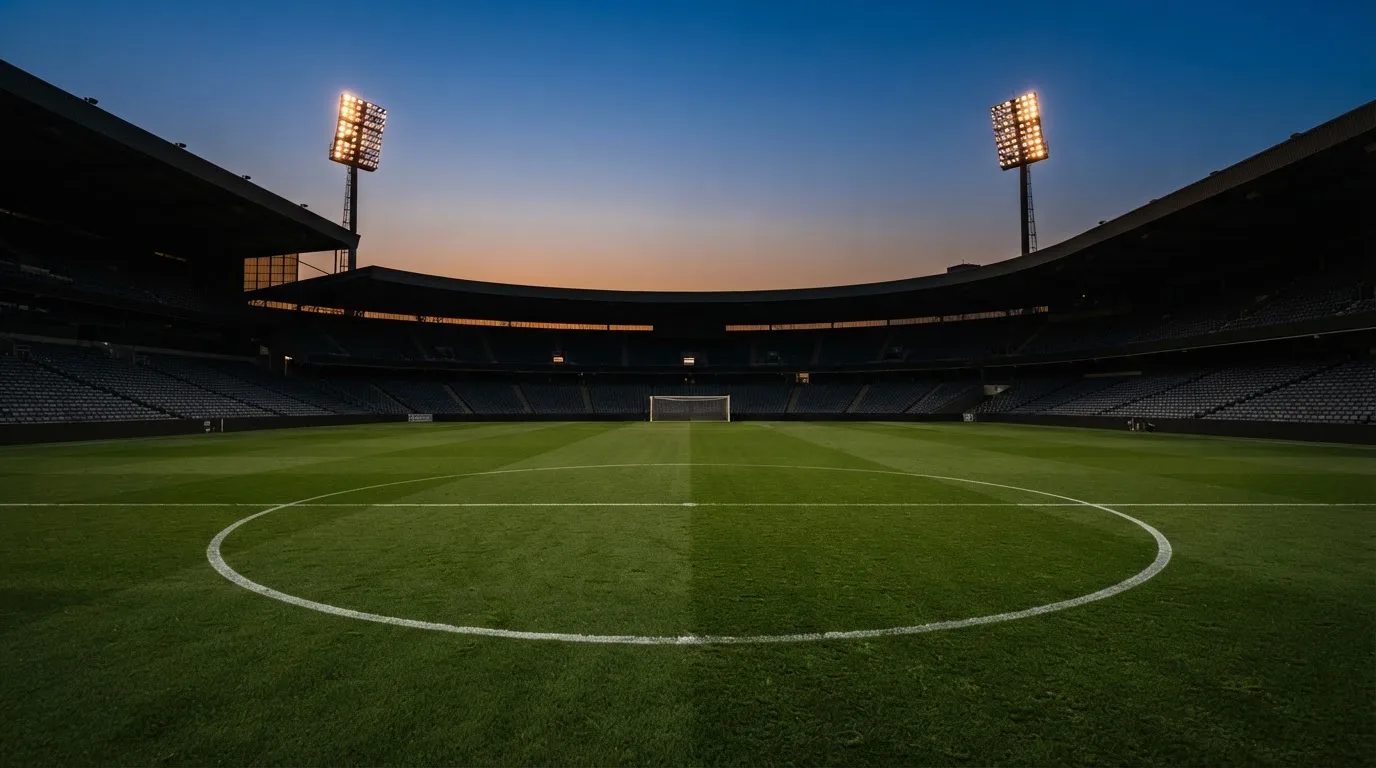 An empty football stadium with floodlight masts at dusk