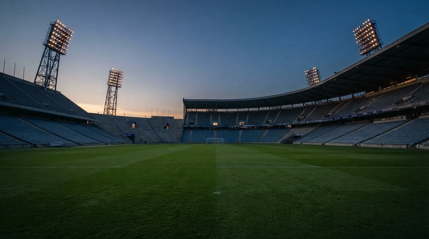 An empty football stadium with floodlight masts at dusk