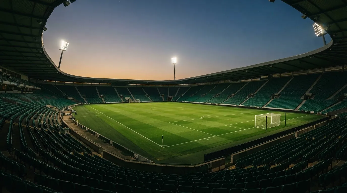 An empty football stadium with floodlight masts at dusk