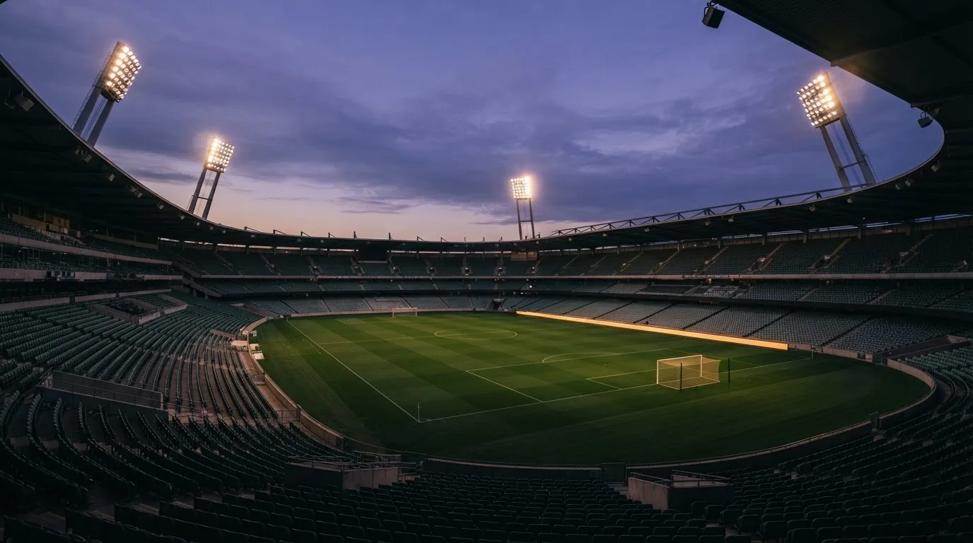 An empty football stadium with floodlight masts at dusk