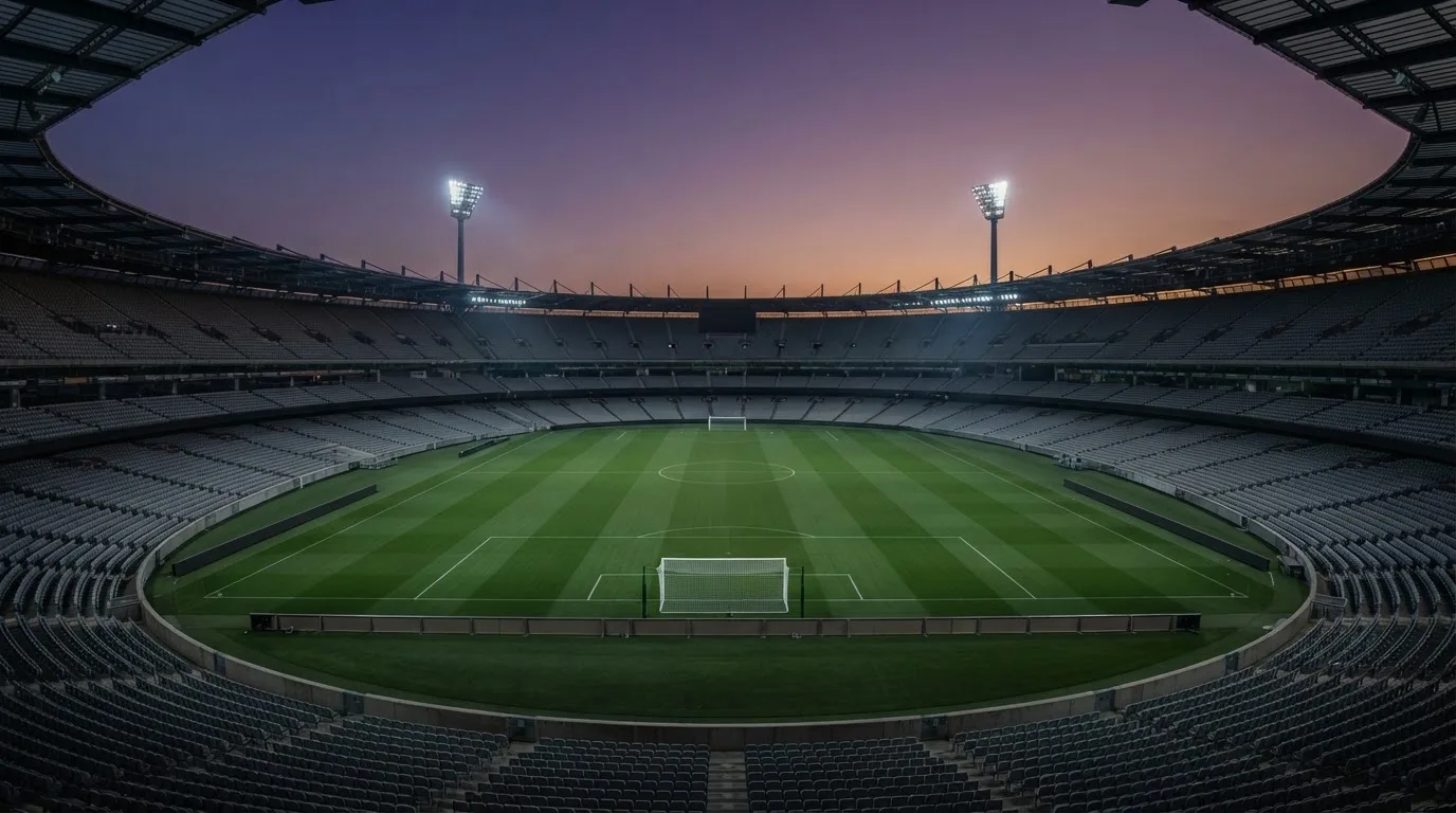 An empty football stadium with floodlight masts at dusk