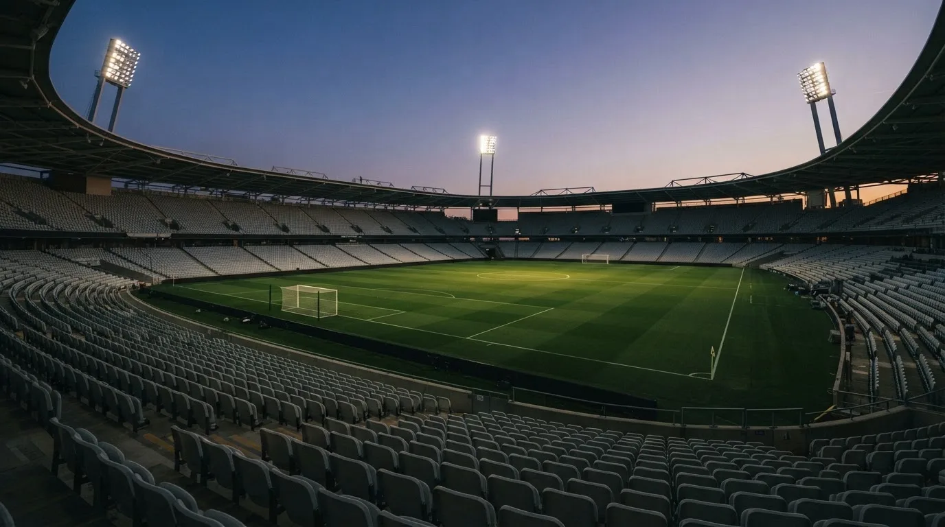 An empty football stadium with floodlight masts at dusk