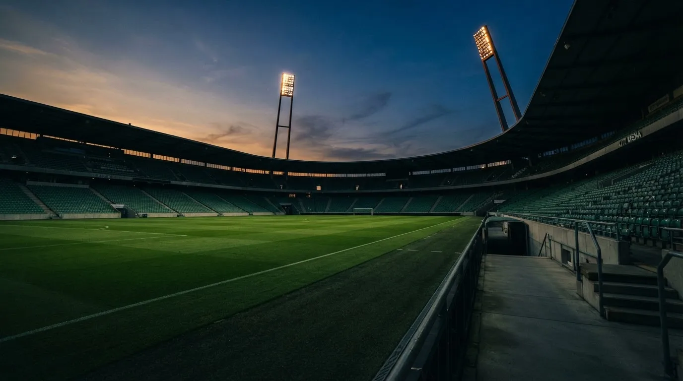An empty football stadium with floodlight masts at dusk