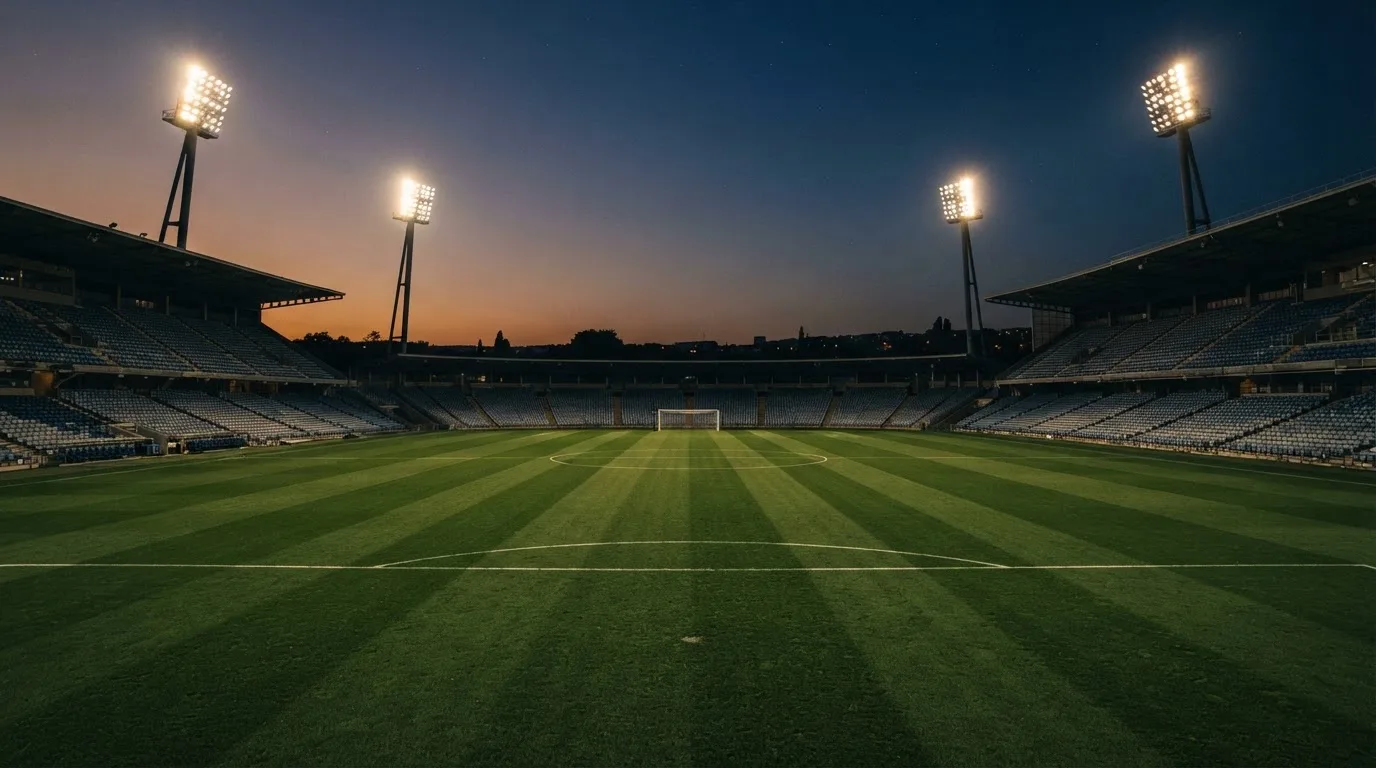 An empty football stadium with floodlight masts at dusk